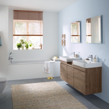 Obiteljska kupaonica sa svjetloplavim zidom i kupaonskim namještajem od karije, elementom s ogledalom, tipkom za aktiviranje i sanitarnom keramikom proizvođača Geberit